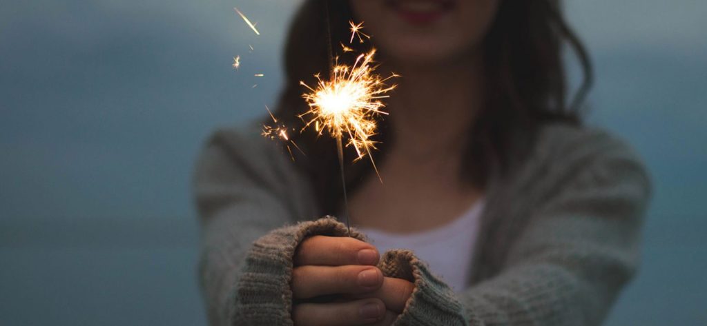 Close up of a lit sparkler in the hands of a young woman at dusk.